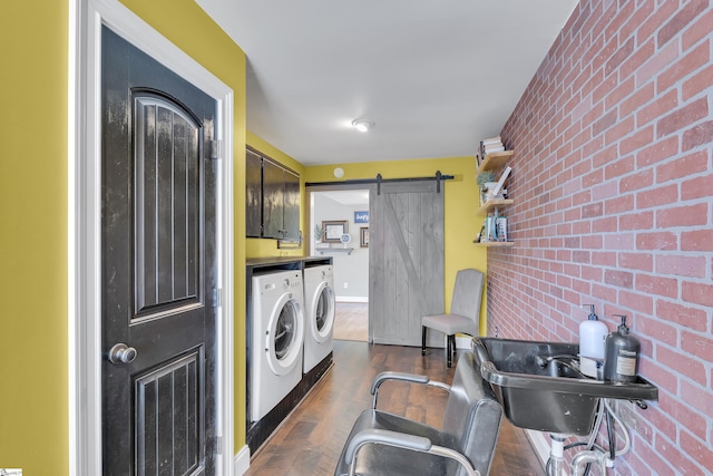 clothes washing area with washing machine and clothes dryer, a barn door, brick wall, and dark wood-type flooring