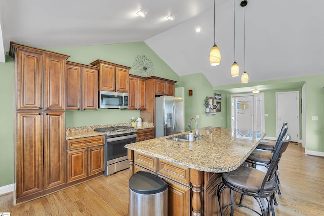 kitchen with stainless steel appliances, a sink, brown cabinetry, a kitchen bar, and an island with sink