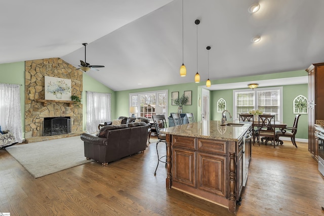 kitchen featuring vaulted ceiling, a sink, ceiling fan, light stone counters, and a fireplace
