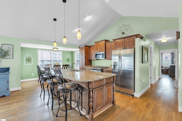 kitchen with appliances with stainless steel finishes, a kitchen breakfast bar, brown cabinets, light stone counters, and an island with sink
