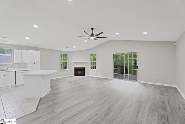 338 E Celestial Dr, Greer, SC 29651 - unfurnished living room with a ceiling fan, a sink, vaulted ceiling, light wood-type flooring, and a warm lit fireplace