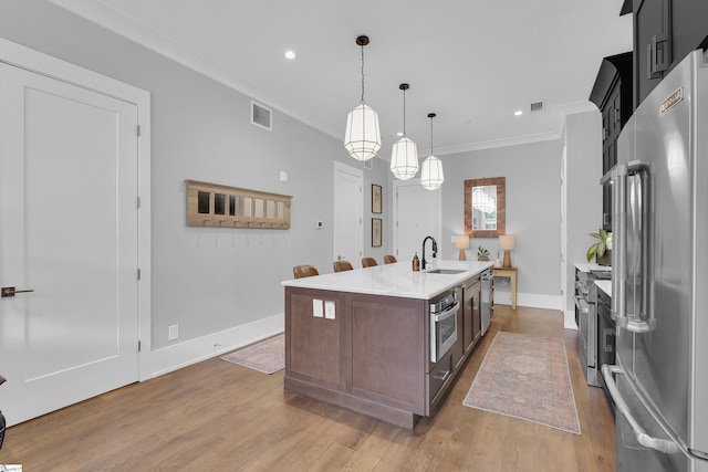 kitchen featuring appliances with stainless steel finishes, a sink, ornamental molding, an island with sink, and hanging light fixtures