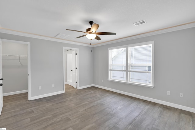 unfurnished bedroom with ornamental molding, wood finished floors, a walk in closet, baseboards, and a closet