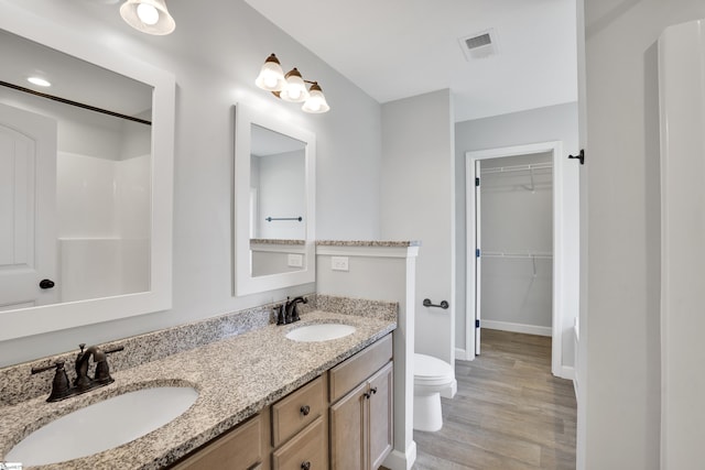 bathroom featuring toilet, wood finished floors, double vanity, baseboards, and a walk in closet