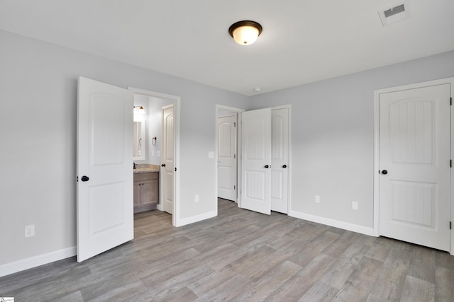 unfurnished bedroom featuring baseboards, light wood-style floors, and ensuite bath