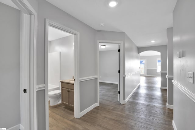 hall with arched walkways, dark wood finished floors, baseboards, and recessed lighting