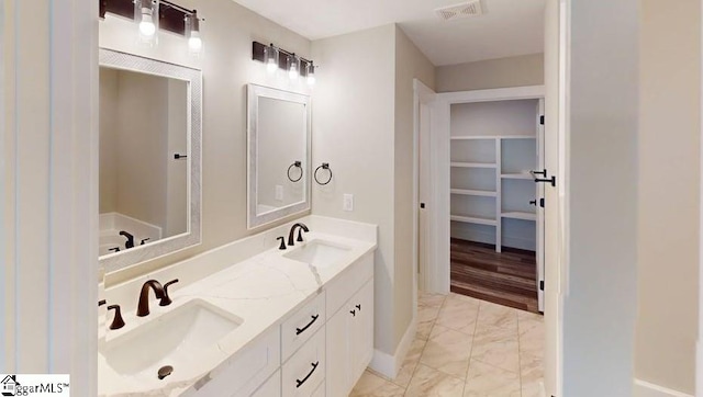 full bath featuring marble finish flooring, baseboards, a spacious closet, and double vanity
