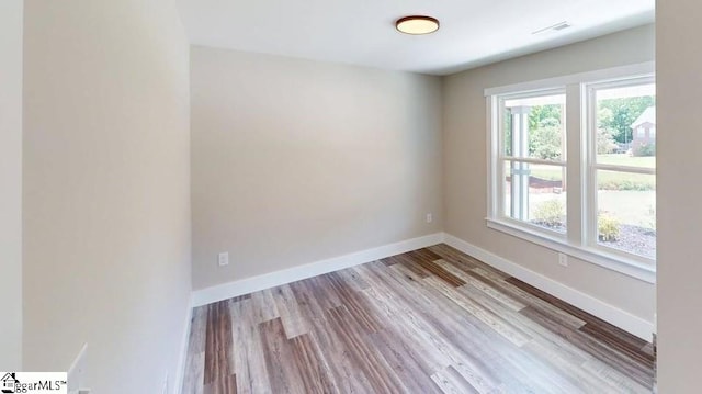 empty room with healthy amount of natural light, wood finished floors, and baseboards