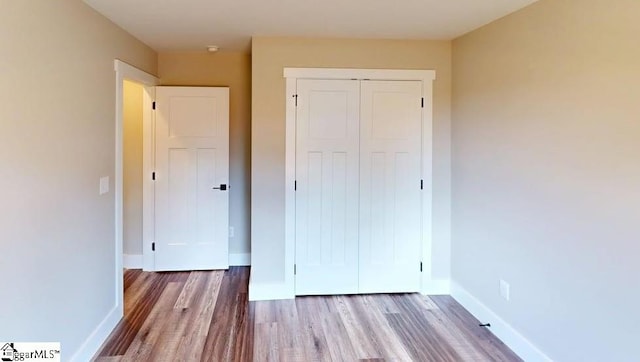 unfurnished bedroom with wood finished floors, a closet, and baseboards