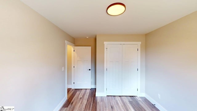 unfurnished bedroom with wood finished floors, baseboards, and a closet