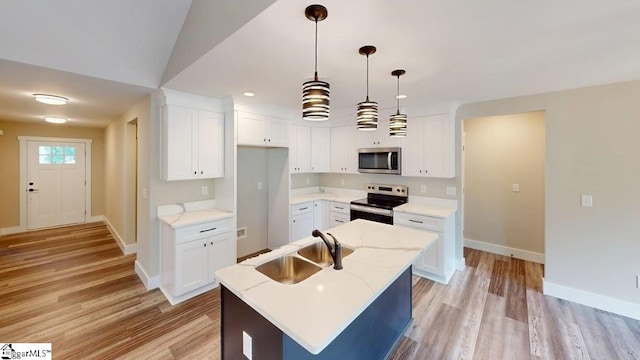 kitchen with appliances with stainless steel finishes, a sink, baseboards, light wood finished floors, and a kitchen island with sink