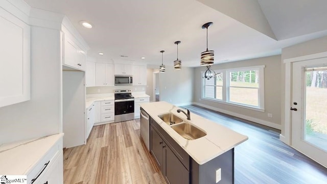 kitchen featuring appliances with stainless steel finishes, a sink, a center island with sink, light wood-style flooring, and white cabinets