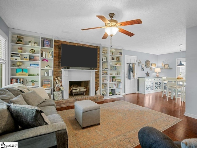 living room with wood finished floors, a ceiling fan, a textured ceiling, baseboards, and a brick fireplace