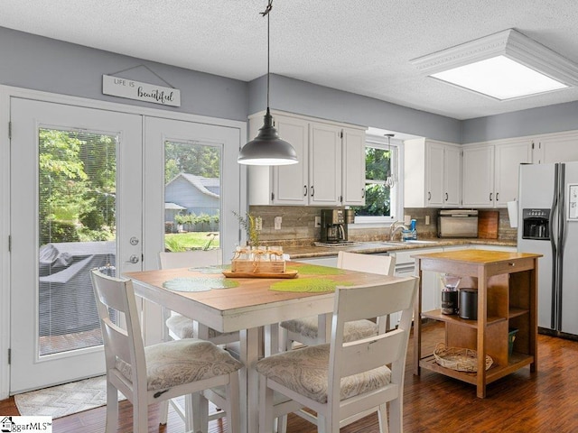 kitchen featuring refrigerator with ice dispenser, a sink, backsplash, white cabinetry, and a textured ceiling