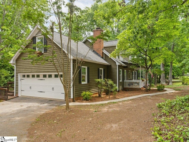 view of front of property with a chimney, asphalt driveway, roof with shingles, an attached garage, and covered porch