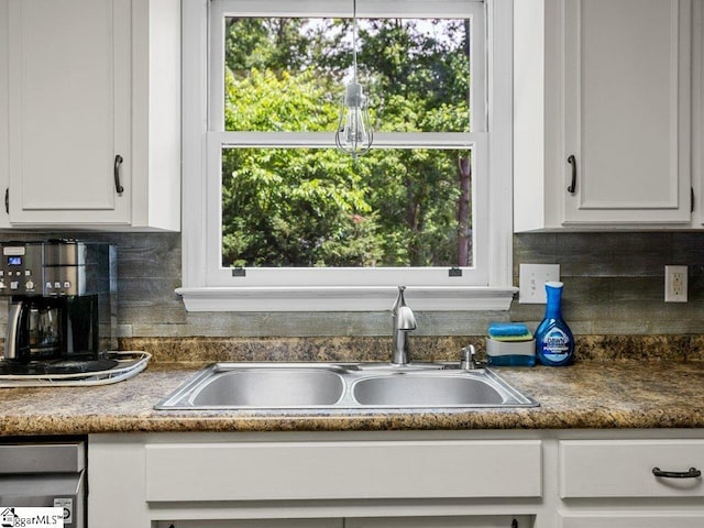 kitchen view of a sink, white cabinets, backsplash, and dark countertops