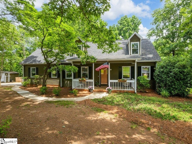 cape cod house with covered porch, a shingled roof, and an outbuilding