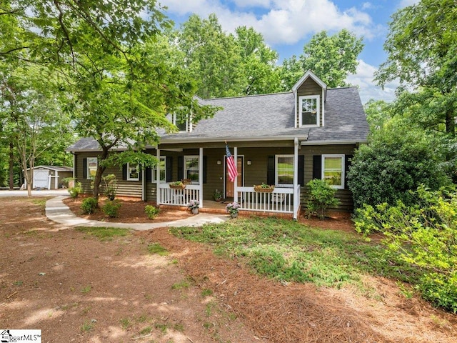 view of front facade featuring a porch, a shingled roof, and an outbuilding