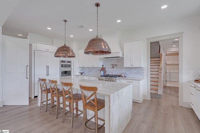 320 Terry Rd, Fountain Inn, SC 29644 - kitchen with washing machine and clothes dryer, premium range hood, white cabinetry, tasteful backsplash, and light wood-type flooring