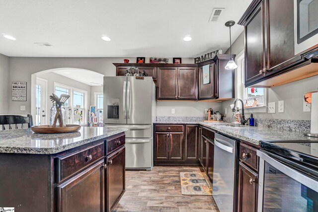 105 Devonfield Dr, Greer, SC 29651 - kitchen featuring appliances with stainless steel finishes, arched walkways, light wood finished floors, light stone countertops, and dark brown cabinetry