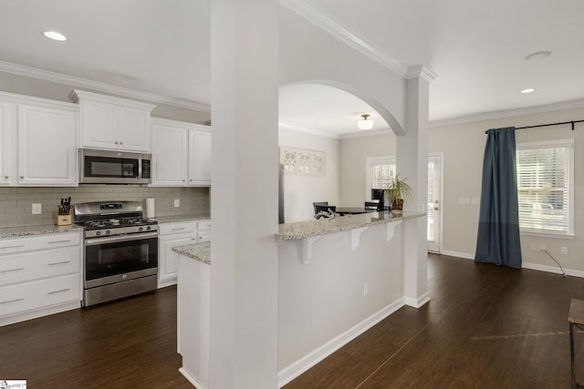 352 Avendell Dr, Easley, SC 29642 - kitchen featuring appliances with stainless steel finishes, arched walkways, dark wood-style floors, a breakfast bar, and decorative backsplash