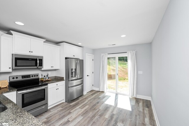 216 Country Gln, Pelzer, SC 29669 - kitchen featuring appliances with stainless steel finishes, baseboards, dark stone counters, white cabinets, and light wood-type flooring