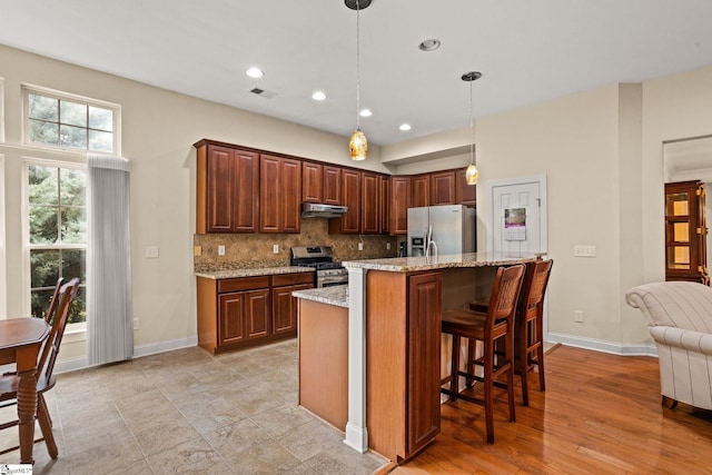 27 Grossmont Dr, Fountain Inn, SC 28644 - kitchen with appliances with stainless steel finishes, under cabinet range hood, tasteful backsplash, light stone countertops, and hanging light fixtures