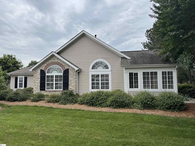 view of front of home featuring a front lawn, stone siding, and a shingled roof
