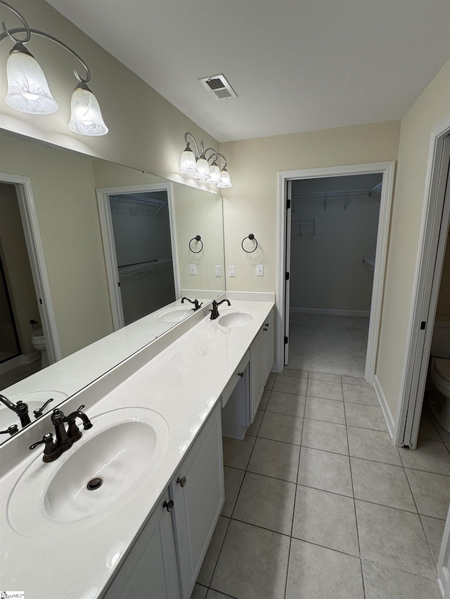 full bathroom featuring toilet, double vanity, a walk in closet, and tile patterned flooring