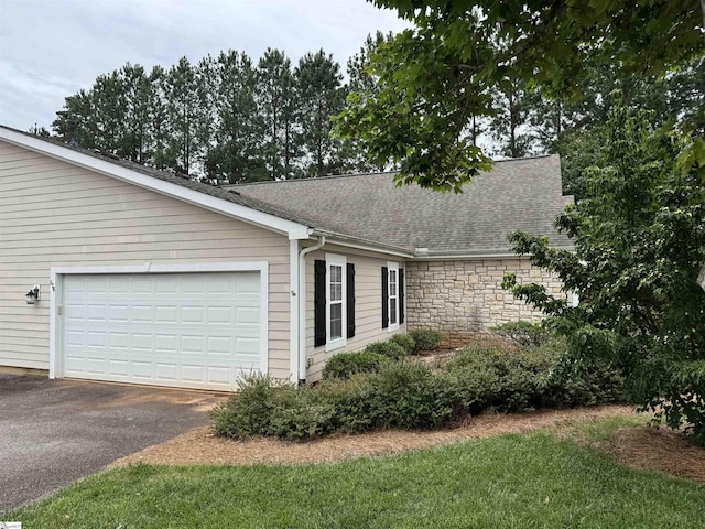view of side of home with asphalt driveway, a shingled roof, an attached garage, and stone siding