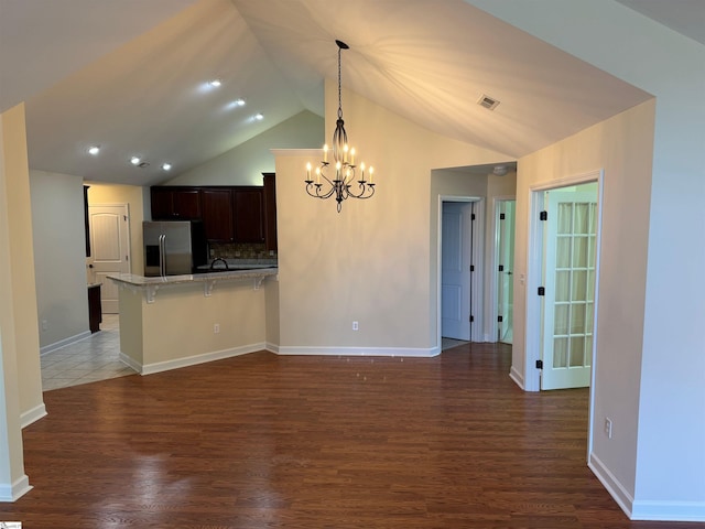kitchen with stainless steel refrigerator with ice dispenser, a chandelier, a peninsula, lofted ceiling, and a breakfast bar area