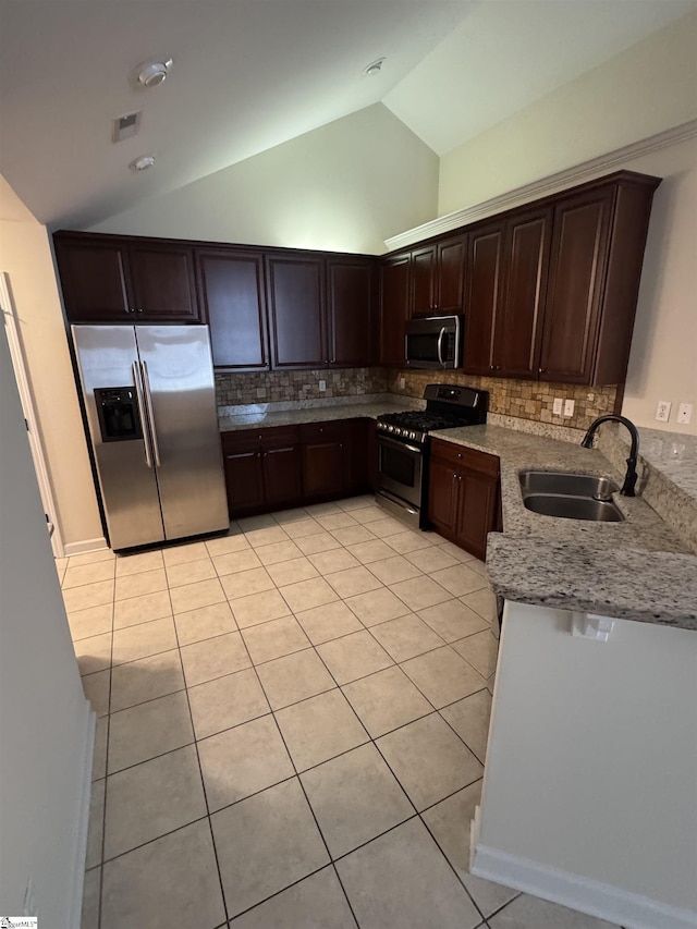 kitchen featuring appliances with stainless steel finishes, a sink, vaulted ceiling, light tile patterned floors, and light stone counters