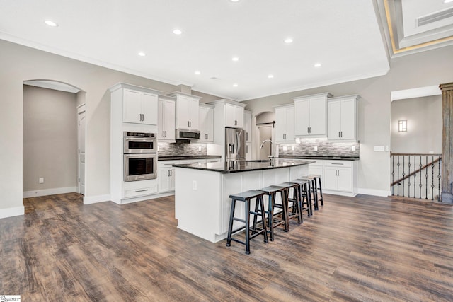 1061 Hidden Glory Dr, Landrum, SC 29356 - kitchen featuring appliances with stainless steel finishes, dark countertops, crown molding, arched walkways, and a kitchen breakfast bar