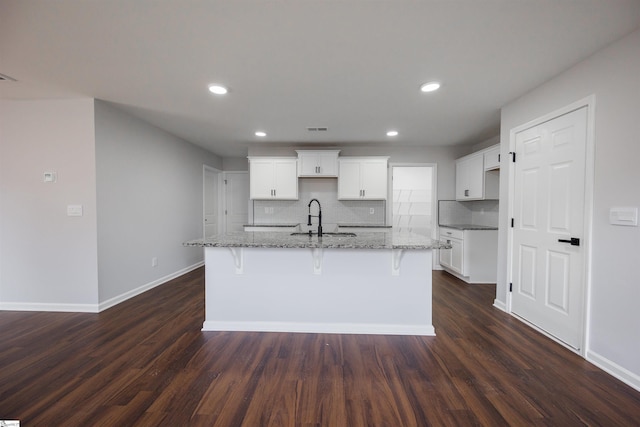 1305 Ledsham Ct, Greer, SC 29651 - kitchen featuring a sink, a kitchen island with sink, decorative backsplash, light stone countertops, and dark wood-style flooring