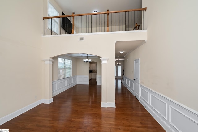 101 Kings Heath Ln, Simpsonville, SC 29680 - unfurnished living room featuring arched walkways, a decorative wall, ornate columns, a chandelier, and wood finished floors