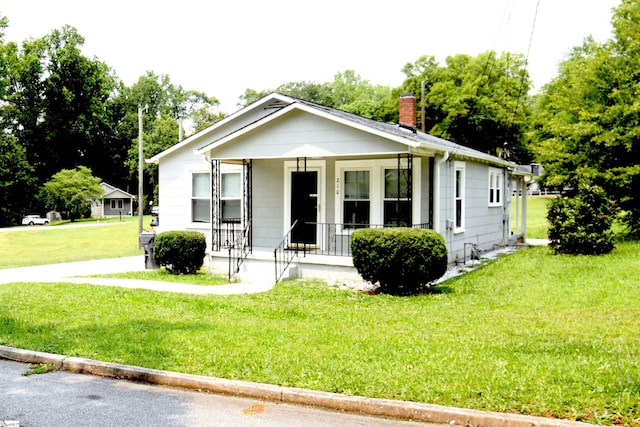 210 Mcdowell St, Laurens, SC 29360 - bungalow with covered porch, a chimney, a front lawn, and view of wooded area