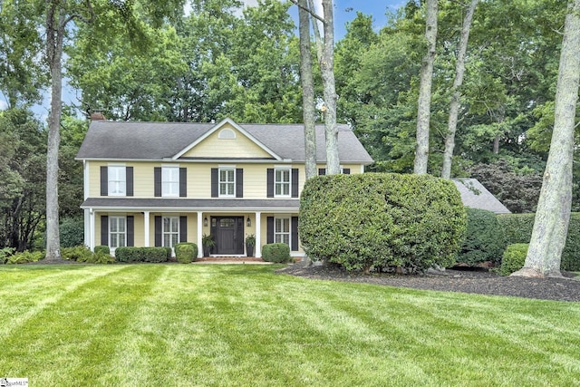103 Brandon Way, Simpsonville, SC 29681 - colonial inspired home with a front yard, a chimney, covered porch, a shingled roof, and view of wooded area