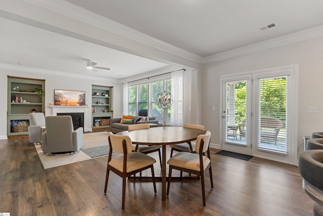 712 Paxton Rose Dr, Greer, SC 29650 - dining space featuring a glass covered fireplace, crown molding, built in shelves, dark wood finished floors, and ceiling fan