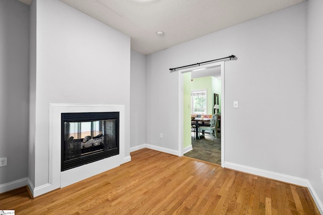 1847 Bertha Knight Rd, Lancaster, SC 29720 - unfurnished living room with light wood finished floors, baseboards, a multi sided fireplace, and a textured ceiling