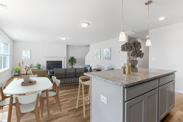 474 Grantham Ct, Spartanburg, SC 29303 - kitchen featuring gray cabinets, light wood finished floors, a kitchen island, hanging light fixtures, and a glass covered fireplace