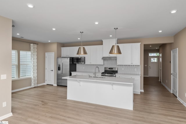 6010 Ives Ave, Spartanburg, SC 29307 - kitchen featuring appliances with stainless steel finishes, light countertops, light wood-type flooring, tasteful backsplash, and a kitchen island with sink