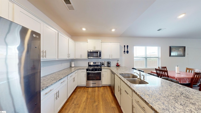 931 Brynderwen Pl, Lyman, SC 29365 - kitchen with stainless steel appliances, a sink, decorative backsplash, white cabinetry, and light wood finished floors