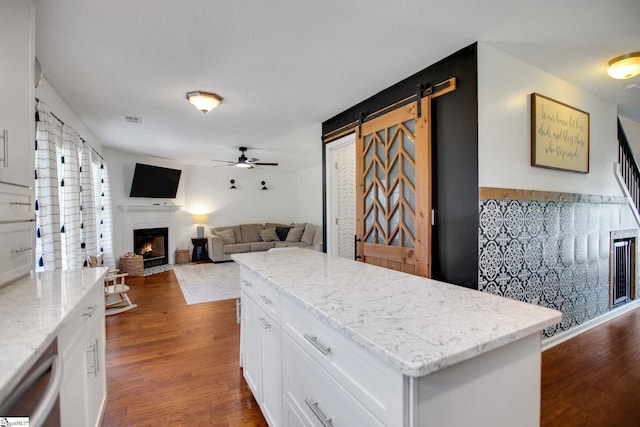 101 Bitternut Ln, Taylors, SC 29687 - kitchen featuring a ceiling fan, white cabinetry, a barn door, a warm lit fireplace, and dark wood-style flooring