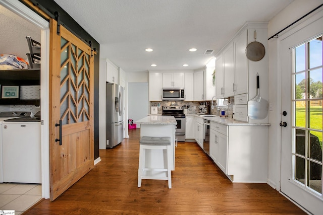 101 Bitternut Ln, Taylors, SC 29687 - kitchen featuring appliances with stainless steel finishes, separate washer and dryer, a barn door, backsplash, and white cabinetry