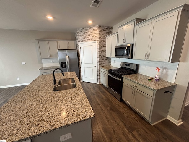 63 Oak Edge Ln, Greer, SC 29651 - kitchen featuring appliances with stainless steel finishes, dark wood finished floors, backsplash, a kitchen island with sink, and light stone countertops