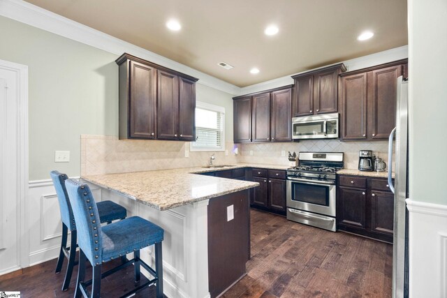 415 Bridge Crossing Dr, Simpsonville, SC 29681 - kitchen featuring appliances with stainless steel finishes, a peninsula, dark brown cabinetry, crown molding, and dark wood-style flooring