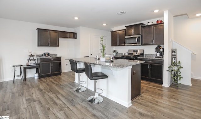 1421 Trotting Ave, Roebuck, SC 29376 - kitchen with stainless steel appliances, wood finished floors, dark brown cabinetry, a kitchen bar, and light stone countertops