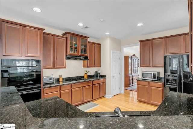 109 Amberleaf Way, Simpsonville, SC 29681 - kitchen with black appliances, under cabinet range hood, light wood-type flooring, dark stone counters, and glass insert cabinets