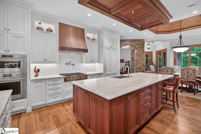 915 Rippling Water Way, Salem, SC 29676 - kitchen featuring premium range hood, arched walkways, stainless steel appliances, light wood finished floors, and glass insert cabinets
