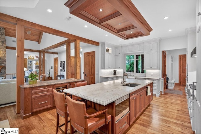 915 Rippling Water Way, Salem, SC 29676 - kitchen with stainless steel microwave, a kitchen island with sink, backsplash, light wood-style flooring, and beam ceiling